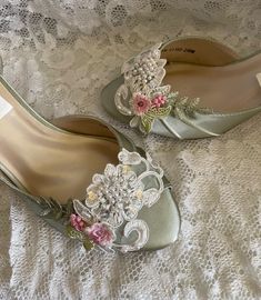 two pairs of shoes with flowers on them sitting on a lace covered bed sheet, one is green and the other is white