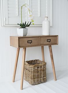 a wooden table with two drawers and a basket on it next to a white wall