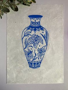 a blue and white vase sitting on top of a piece of paper next to a plant