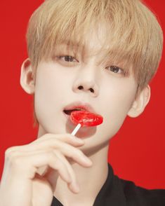 a young man with blonde hair is holding a red lollipop in his mouth