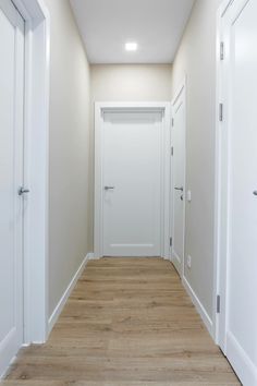 an empty hallway with white doors and wood flooring on both sides, leading to another room