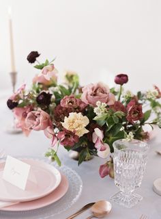 the table is set with pink and white plates, silverware, and floral centerpieces