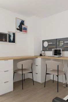 a desk with two chairs and a laptop on top of it in a white room