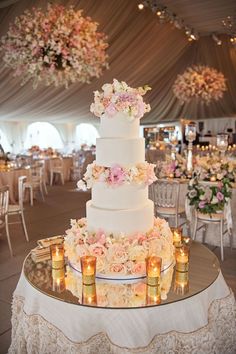 a wedding cake sitting on top of a table covered in white cloths and pink flowers