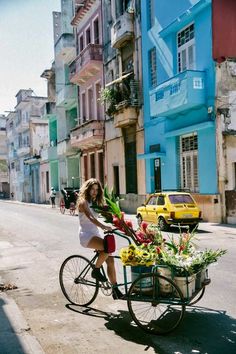 a woman riding a bike with flowers in the basket on the side of the road