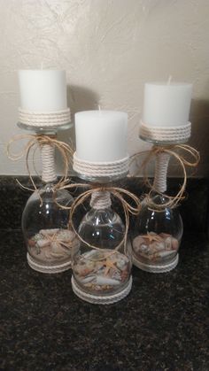 three clear glass vases with seashells in them and two white candles on the side