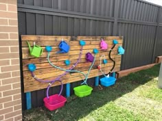 some buckets are hanging on a wooden board outside in the grass and one is painted blue, green, pink and purple