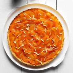 a pie on a white plate topped with sliced peaches and pistachio seeds