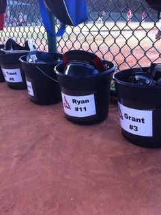 several buckets with baseball equipment in them sitting on the ground next to a fence