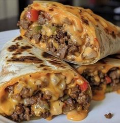 two burritos on a plate with cheese and ground beef in the middle one is cut in half