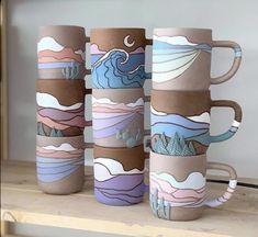 four coffee mugs sitting on top of a wooden shelf with mountains and clouds painted on them