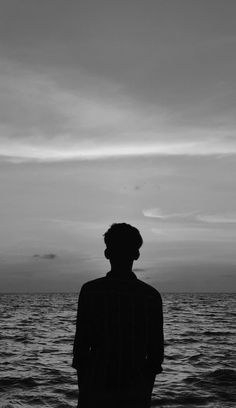 a person standing in front of the ocean looking at the sky with clouds above them