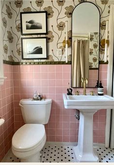 a white toilet sitting next to a sink in a bathroom under a mirror and framed pictures on the wall