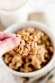 a hand holding a granola in front of a bowl of cereal