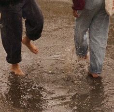 two people are walking in the rain with their feet up and one person is holding an umbrella