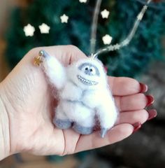 a hand holding a small stuffed animal in front of a christmas tree with snowflakes