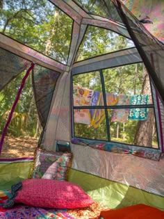 the inside of a tent with pillows and blankets on it's sides, in front of a large window