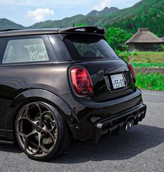 the back end of a mini cooper hatchback on a road with mountains in the background