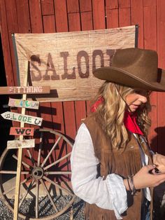 a woman wearing a cowboy hat and holding a cell phone in front of a saloon sign