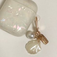 a pearl and gold charm sitting on top of a white table next to an empty container