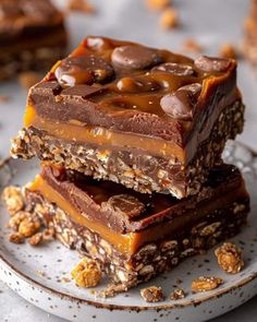 three pieces of chocolate peanut butter fudge bars stacked on top of each other with nuts scattered around them