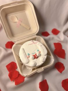 a small cake in a box on a bed with red petals around it and a fork sticking out of the top