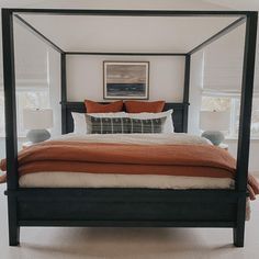 a four poster bed in a bedroom with orange pillows and blankets on top of it