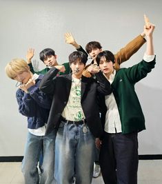 group of young men standing next to each other in front of a wall with their hands up