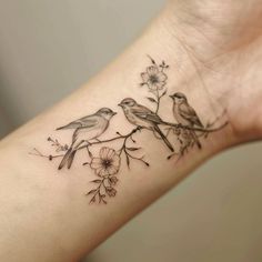 two birds sitting on a branch with flowers and leaves tattooed on the left side of the arm