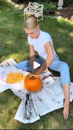 a woman sitting in the grass carving a pumpkin