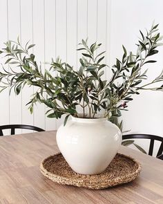 a white vase sitting on top of a wooden table next to a wicker place mat