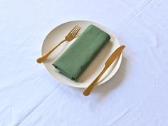 a white plate topped with a green napkin and two golden forks next to a fork