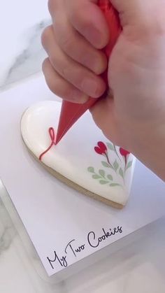 a person is writing on a heart shaped cookie