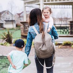 a woman and child walking down a sidewalk with a backpack on their back, holding hands