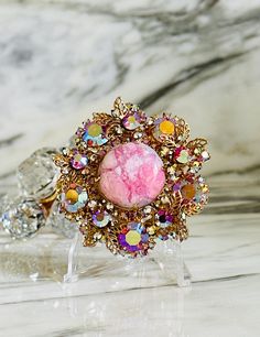 Up for your consideration is this vintage DeLizza & Elster (Juliana) brooch that centerpieces a pink "matrix" cabochon and is surrounded by aurora borealis pink rhinestones and gold tone accent leaves. This D & E brooch also has a pendant bail to adorn a strand of your choice if you prefer to wear it as a necklace.  Unsigned (like all Juliana brooches), but a stunning piece of jewelry history from the 1960s. Condition:  Very good vintage condition, all stones intact and clasp is in wonderful working order. Shows just a bit of wear to the AB coating, but fabulous shape for age. Dimensions:  Approximately 2.25" in diameter FREE SHIPPING via USPS PRIORITY or USPS GROUND ADVANTAGE within the 48 continental states only. All sales are final/no returns... but please contact us if there is an issu Elegant Pink Brooches For Collectors, Vintage Pink Collectible Brooches, Pink Rhinestone Brooches As Gift, Pink Rhinestone Brooches For Gifts, Pink Brooch Jewelry For Wedding, Pink Wedding Brooch Jewelry, Vintage Pink Brooches For Party, Pink Rhinestone Party Brooches, Pink Rhinestone Party Brooch