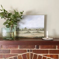 a painting on a mantle next to a vase with a plant in it