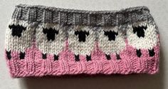 a pink and white knitted hat with black sheeps on the front, sitting on top of a table