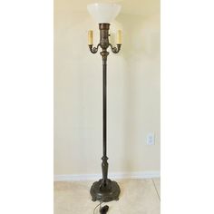 an old fashioned floor lamp with two candles on it's base and a white glass shade