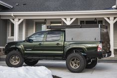 a green truck parked in front of a house with snow on the ground next to it