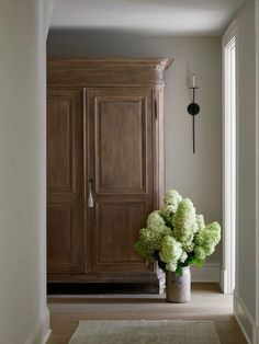 a vase filled with green flowers sitting on top of a wooden floor next to an armoire