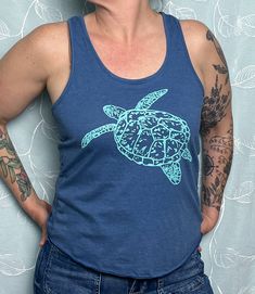 Our hand-drawn Sea Turtle design is printed in teal on this super soft royal blue eco tri-blend racerback tank. Straight through the body. Overlock hem. 40% tencel model (plant fibers), 35% cotton, 25% recycled poly. Sizes available: XS, SM, MED, LRG, XL, 2X.  Runs true to size for form fitting, order up for a looser fit.  Model is a size Medium/ Large and wearing a medium. Our original, hand-drawn designs are printed on sweat-shop free clothing using environmentally conscious water-based inks. Casual Blue Printed Tank Top, Blue Crew Neck Tank Top For Beach, Fitted Casual Tank Top With Screen Print, Casual Fitted Tank Top With Screen Print, Blue Crew Neck Tank Top For The Beach, Printed Blue Cotton Tank Top, Printed Cotton Blue Tank Top, Blue Printed Cotton Tank Top, Blue Graphic Print Racerback Tank Top