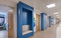 an empty hospital hallway with blue walls and white chairs on either side of the room