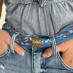 a woman is wearing a blue belt with red and white flowers on it, while holding her hands in her pockets