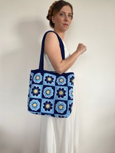 a woman holding a blue and yellow crocheted bag in front of a white wall