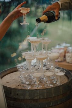 champagne being poured into wine glasses on top of a barrel filled with small white cups