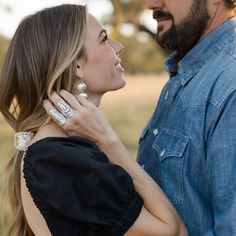 a man and woman standing close to each other in front of a field with trees