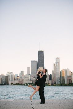 a man and woman kissing on the beach in front of a large cityscape