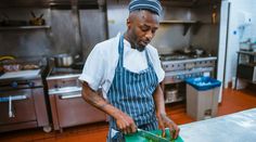 a man in an apron cutting food on a green board