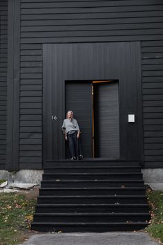 a woman standing in front of a black building with stairs leading up to the door