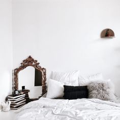 a bed with white sheets and pillows on top of it next to a wooden mirror